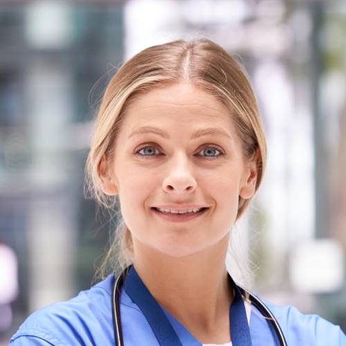 Portrait Of Female Doctor With Stethoscope Wearing Scrubs Standing In Modern Hospital Building